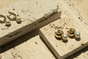 A pair of beautiful gold vermeil pearl huggies sit on a travertine tiles, each piece featuring lustrous pearls from our Broken Bay Pearl Farm shining in the natural light.