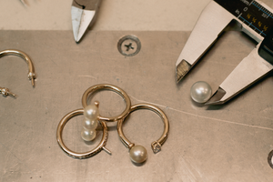 Several hand-crafted pearl rings sit on the jeweller's workshop table, ready to be crafted for a made to order piece.