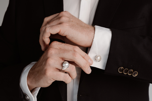 A man dresses in his suit before an event, putting on his Australian South Sea Mabe pearl ring and matching pearl cufflinks.