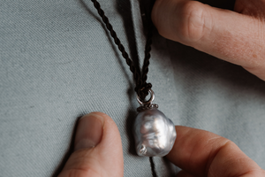 A man holds his stunning pendant that features an Australian South Sea Baroque pearl set alongside black diamonds, and hung on a black silk cord necklace.