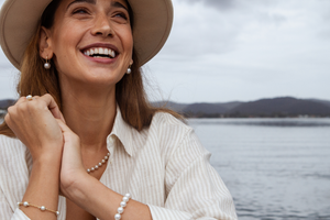A woman broadly smiles wearing her Australian Saltwater pearl jewellery with the Broken Bay Pearl Farm in the background of the photo.