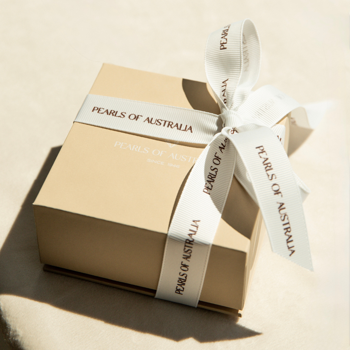 Gift box with a white ribbon labeled 'Pearls of Australia' on a beige background