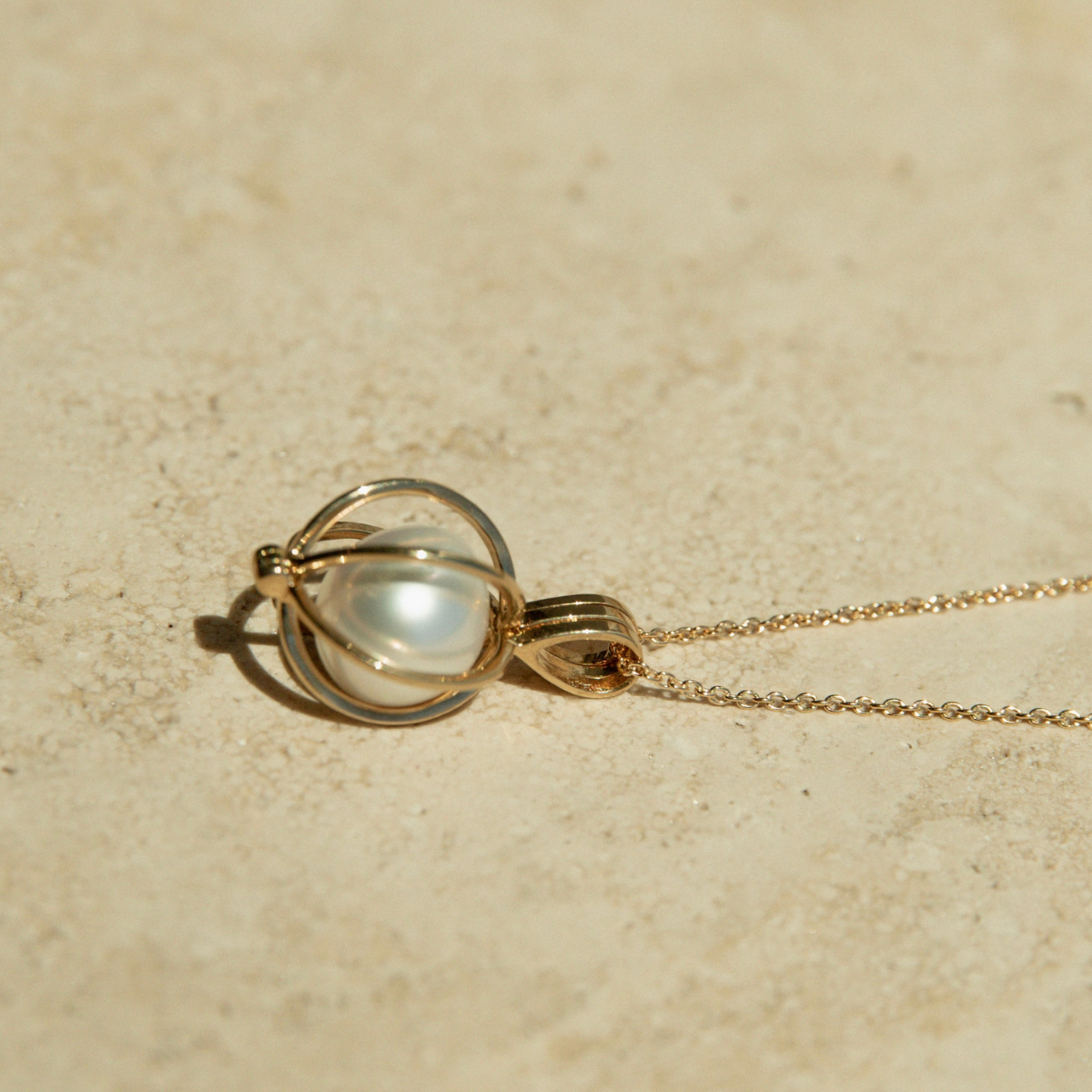 Gold necklace with a pearl pendant on a beige background