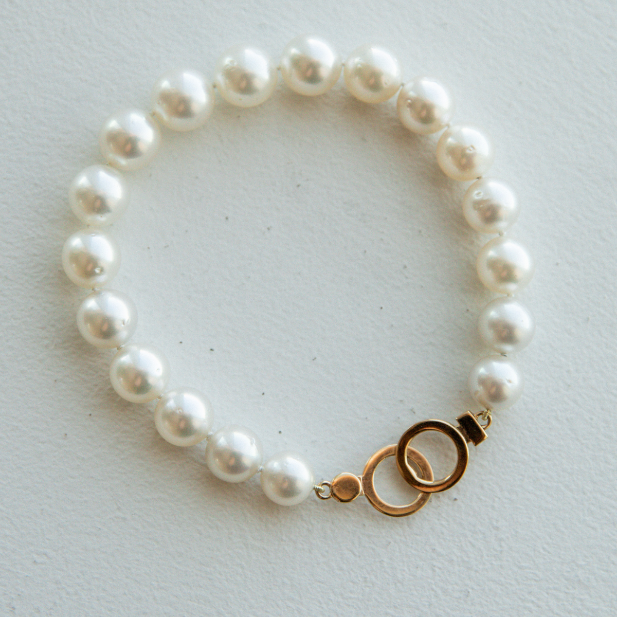 Pearl strand bracelet with a gold circle clasp on a light gray background