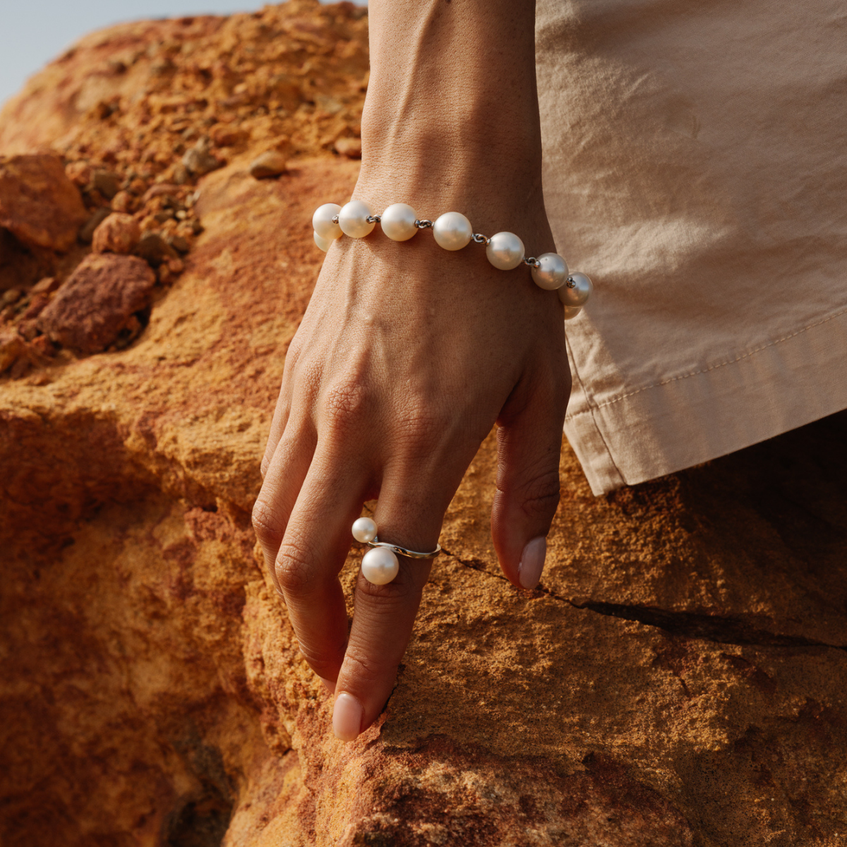 Hand wearing a pearl bracelet and ring against a rocky background