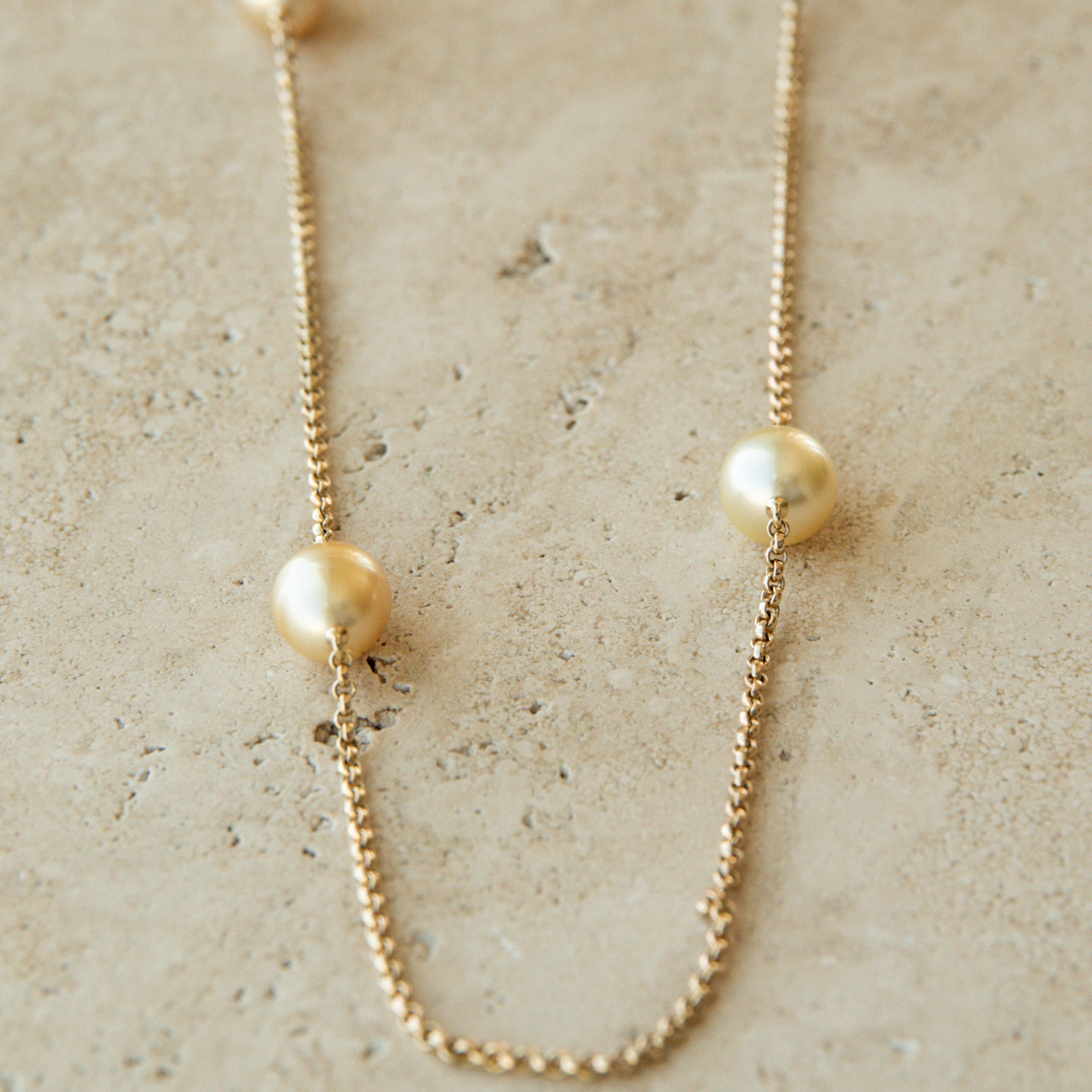 Gold chain necklace with gold pearls on a textured beige surface