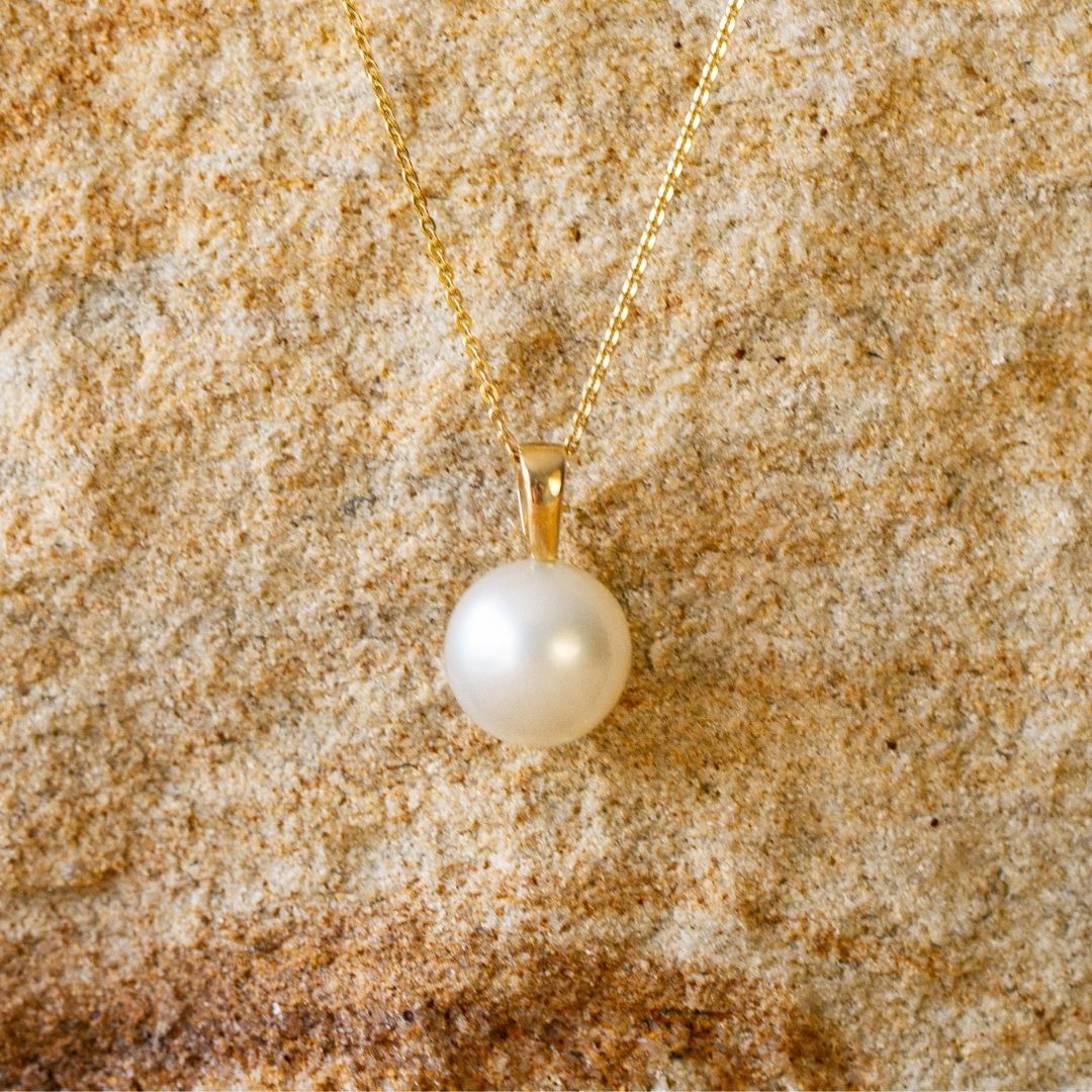 A stunning Cocos Pendant featuring a round Australian South Sea pearl set in gold, and hung from a matching gold chain.