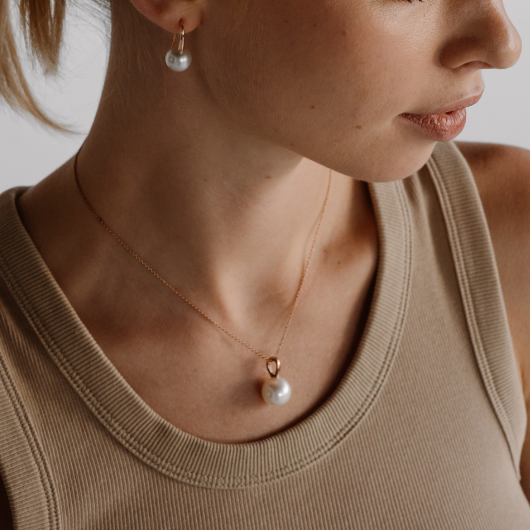 A woman wears her the beautiful Australian South Sea Cocos Pendant featuring a stunning round, white pearl set in gold.