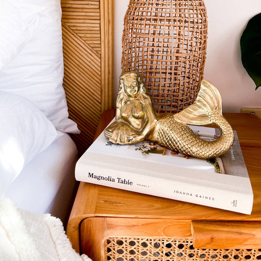 Gold mermaid figurine on a book with a wicker basket in the background
