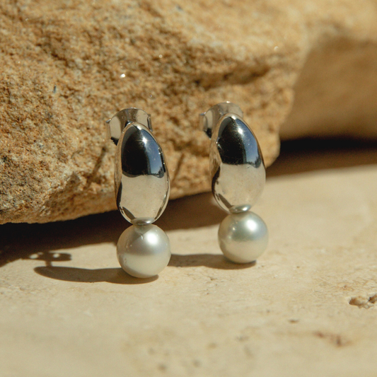 Silver earrings with pearls on a sandy surface