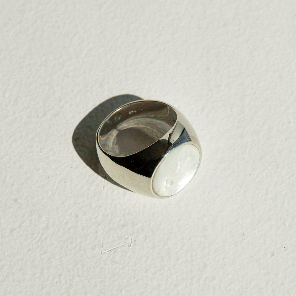 Silver ring set with a Mother of Pearl disc on a light gray background