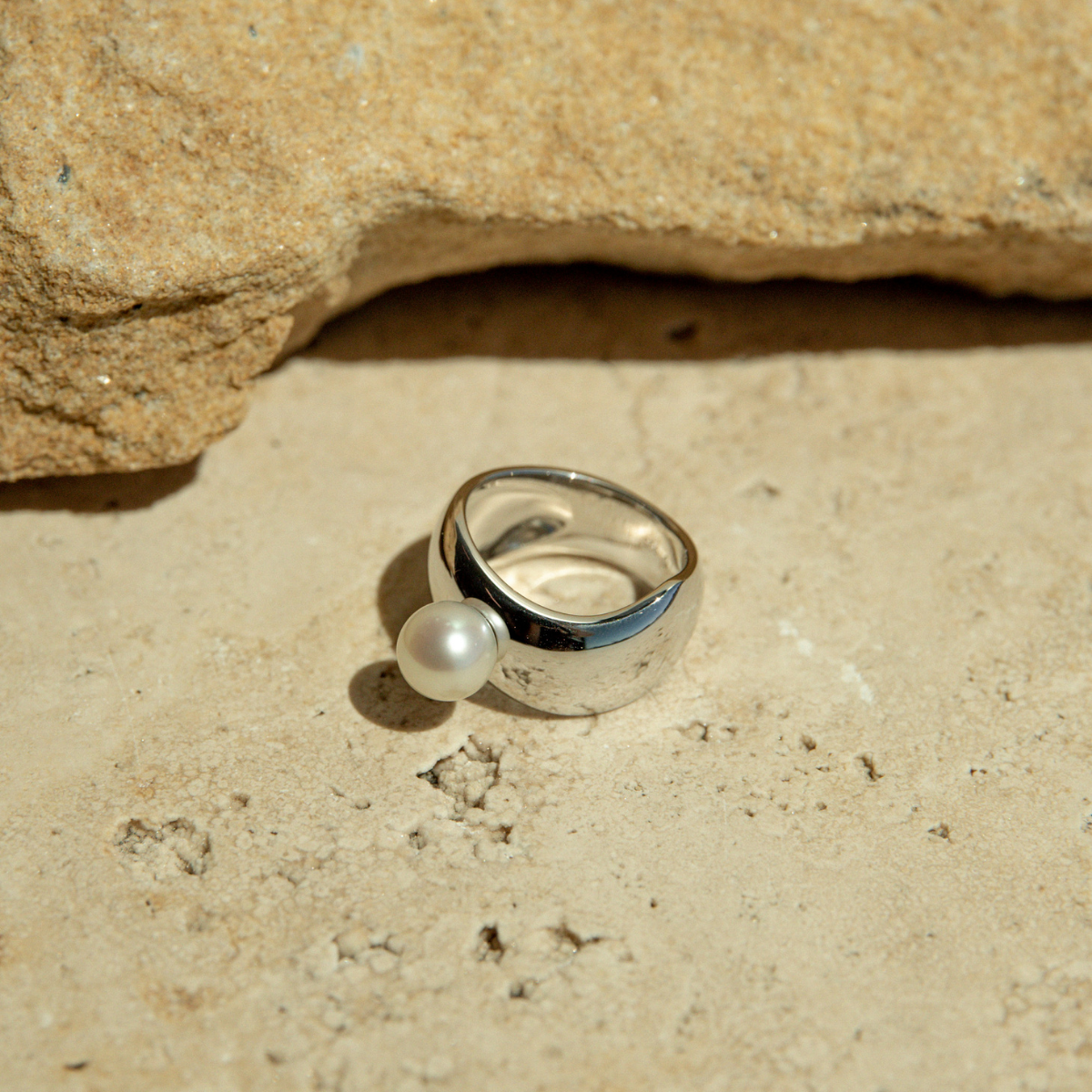 Silver ring with a pearl on a sandy surface