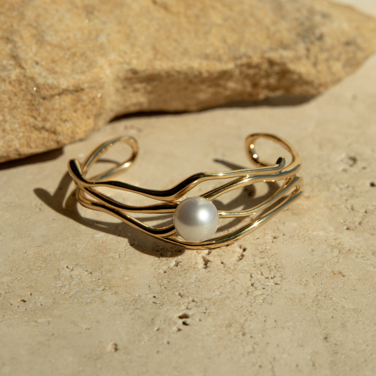 Gold bracelet with a pearl on a sandy surface