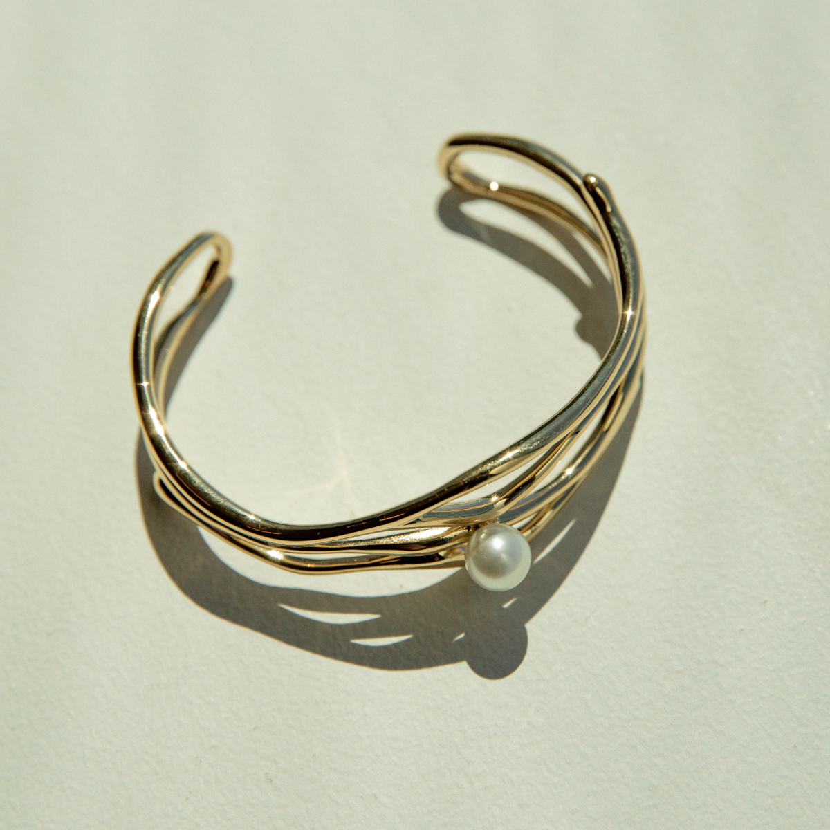 Gold bracelet with a pearl on a light beige background