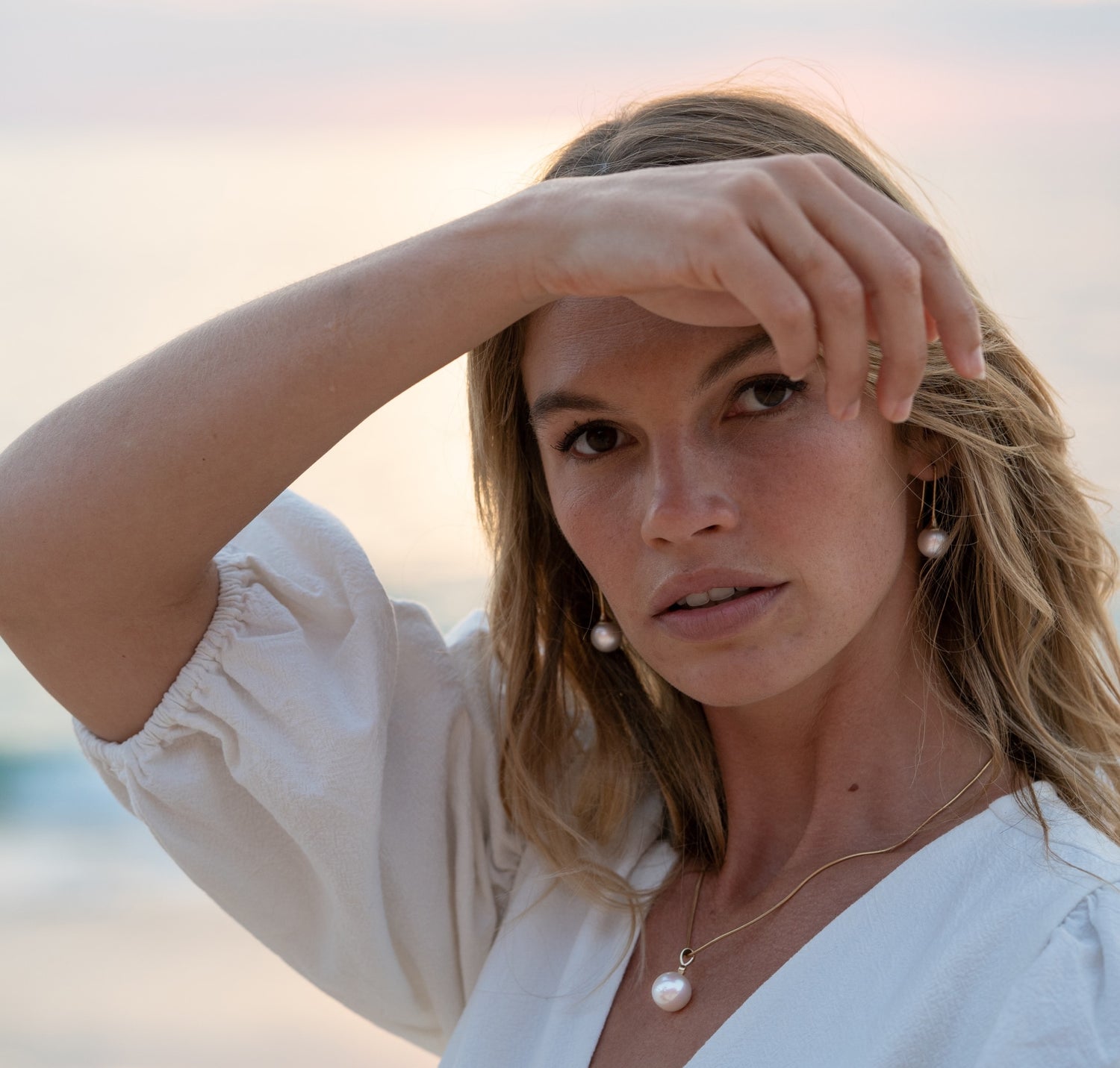 A woman wears her incredible Australian South Sea pearl earrings and pendant, both shining with their innate lustre and set in unique gold designs.