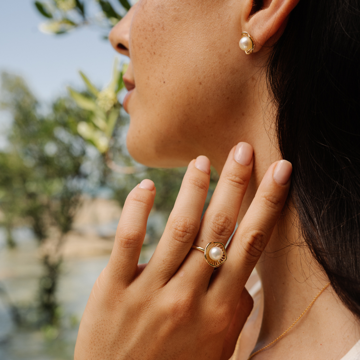 Close-up of a person wearing pearl earrings and ring with a blurred natural background