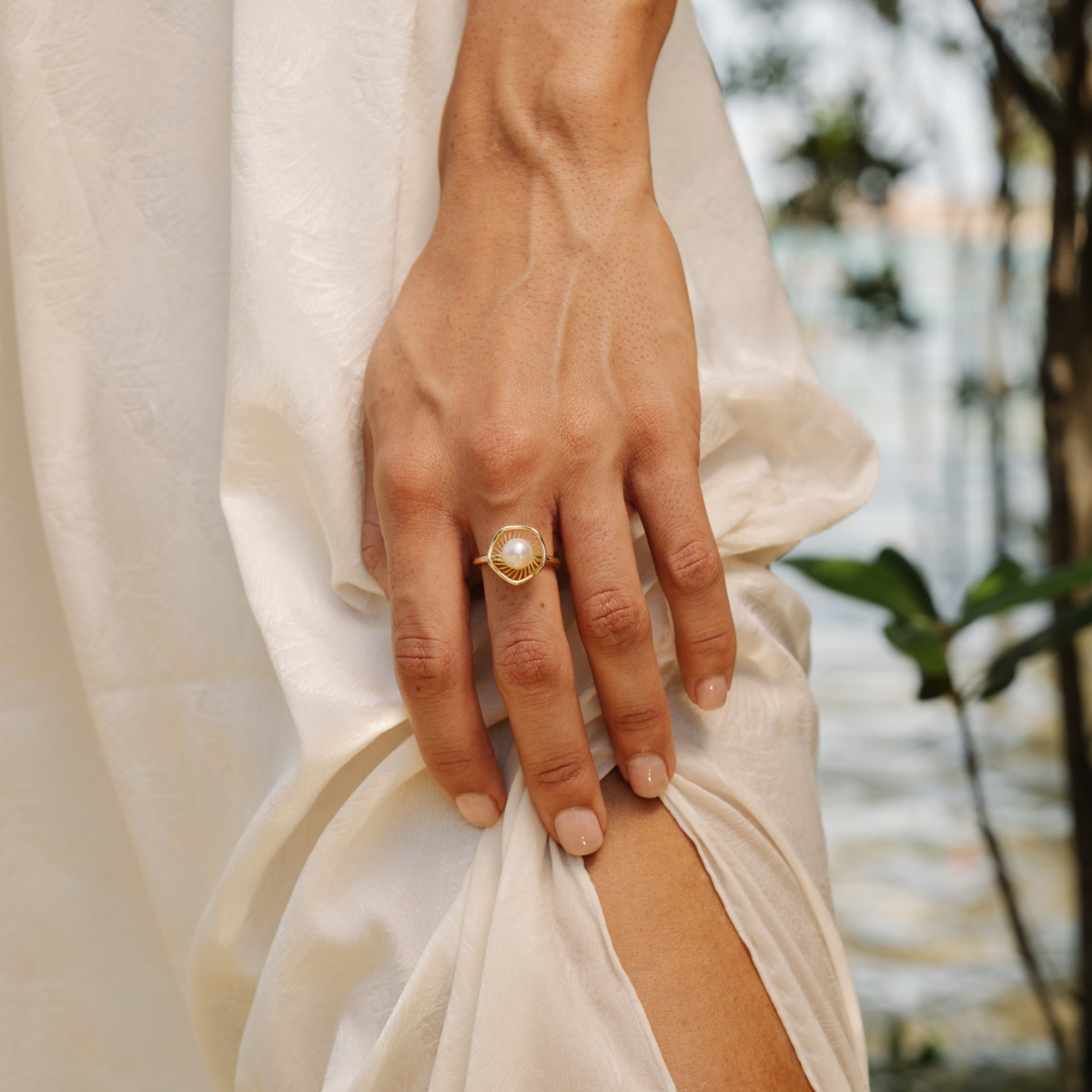 Hand wearing a gold ring with a pearl on a blurred natural background