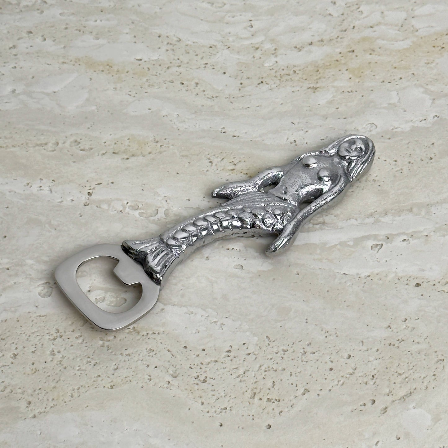 Metallic mermaid bottle opener on a textured surface