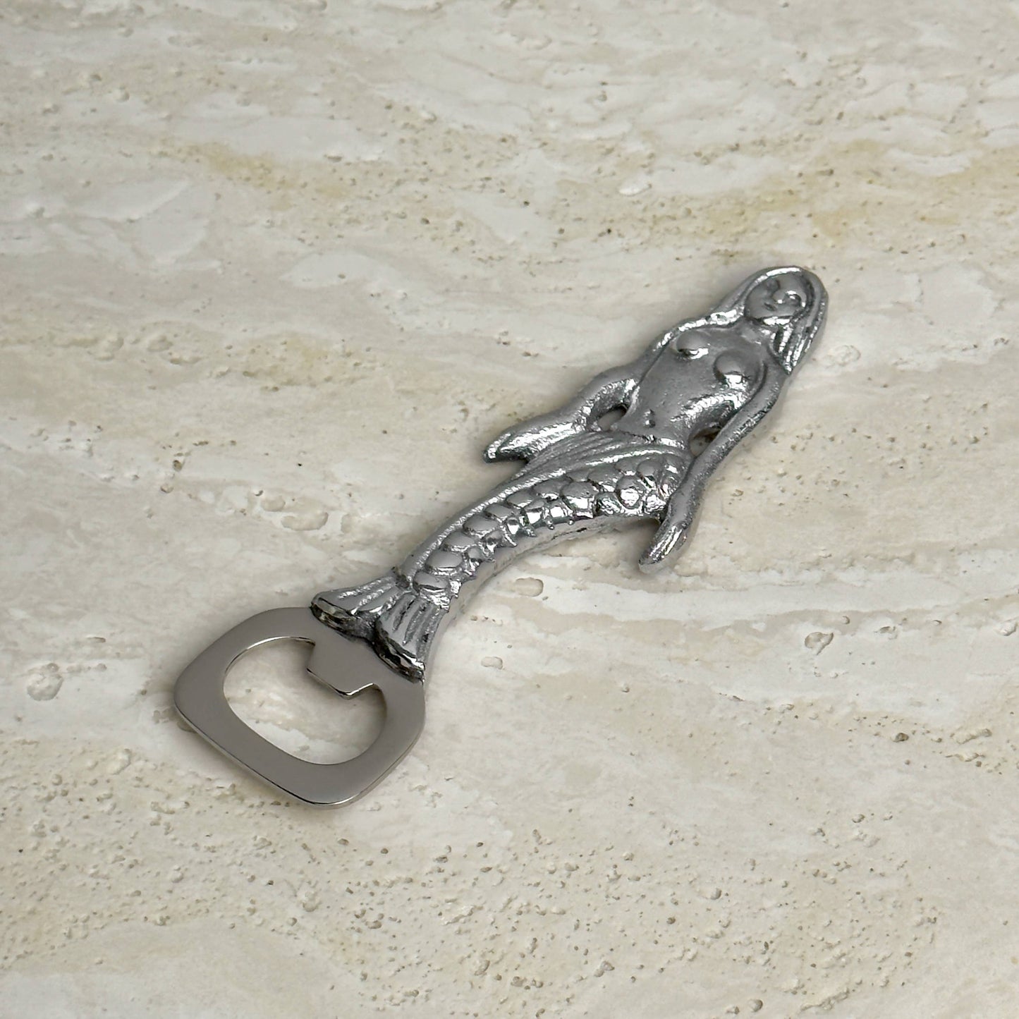 Metallic mermaid shaped bottle opener on a beige stone surface