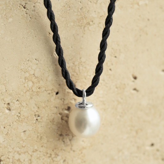 A beautiful Australian South Sea Pearl Charm set in gold sitting on a silk cord rope.