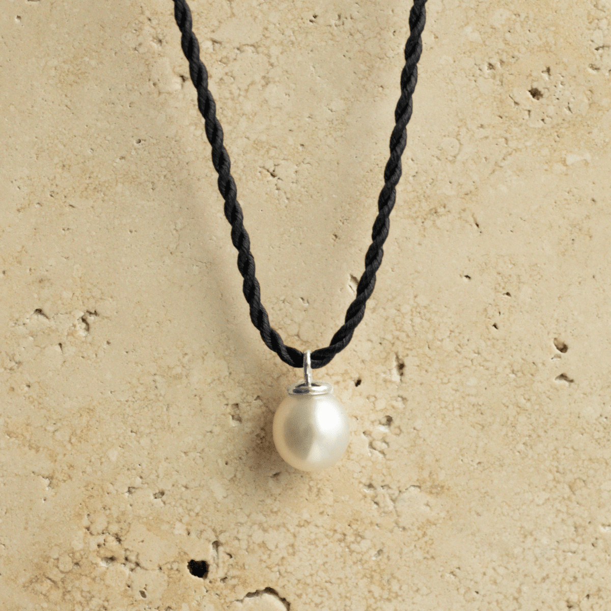 A beautiful Australian South Sea Pearl Charm set in gold sitting on a silk cord rope.