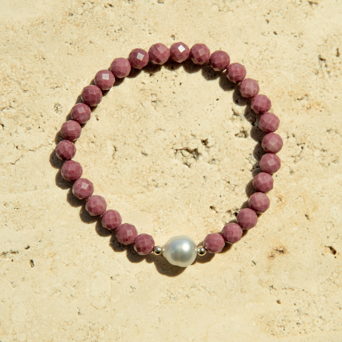 Beaded faceted rhodonite bracelet with an Australian South Sea pearl bead on a textured surface.