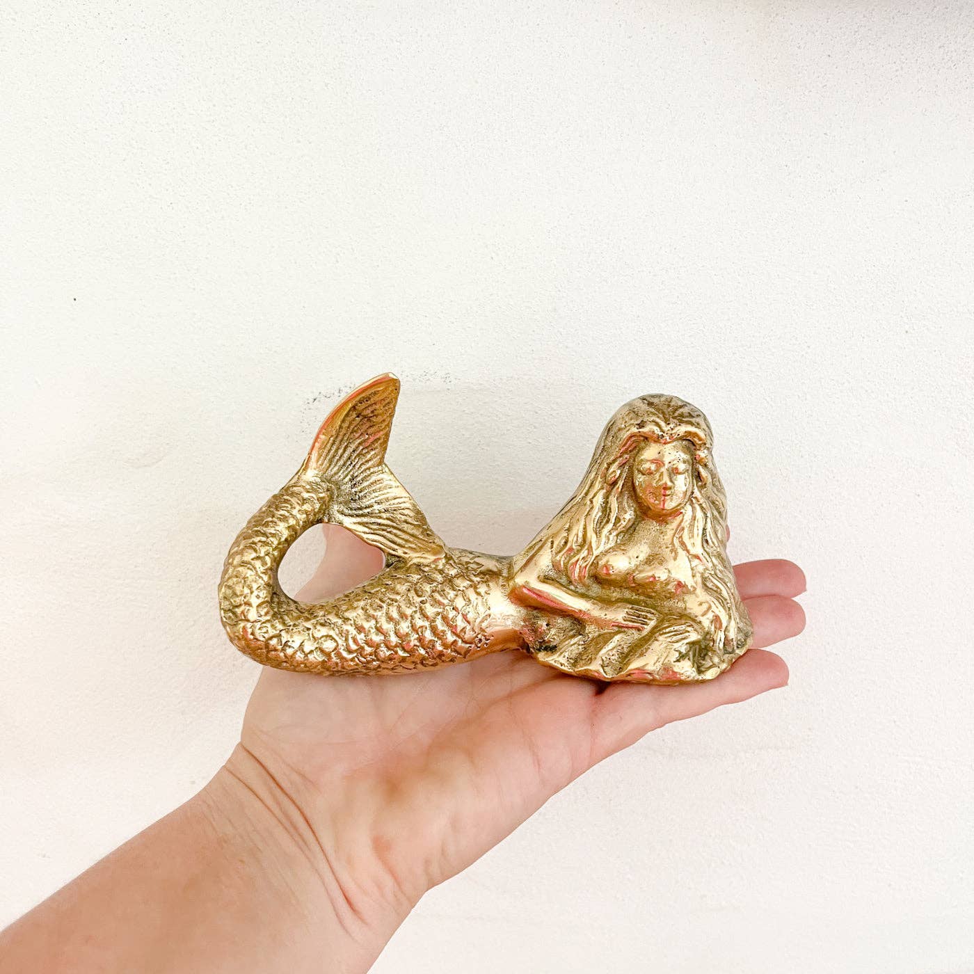 Gold mermaid figurine held in a hand against a white background