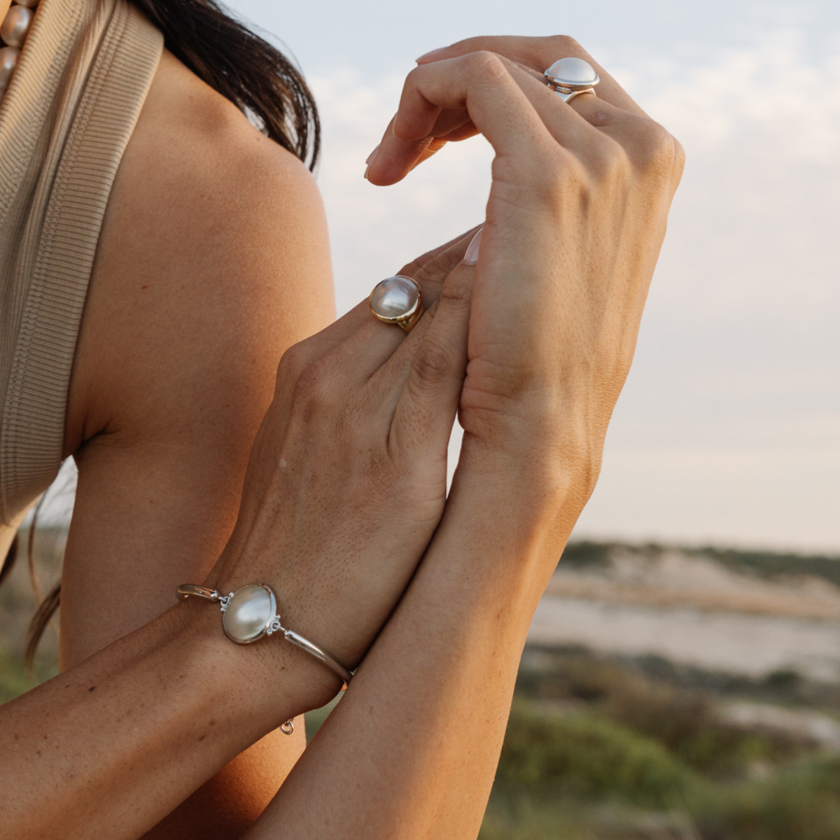 Close-up of two hands with a mabe pearl bracelet against a natural background