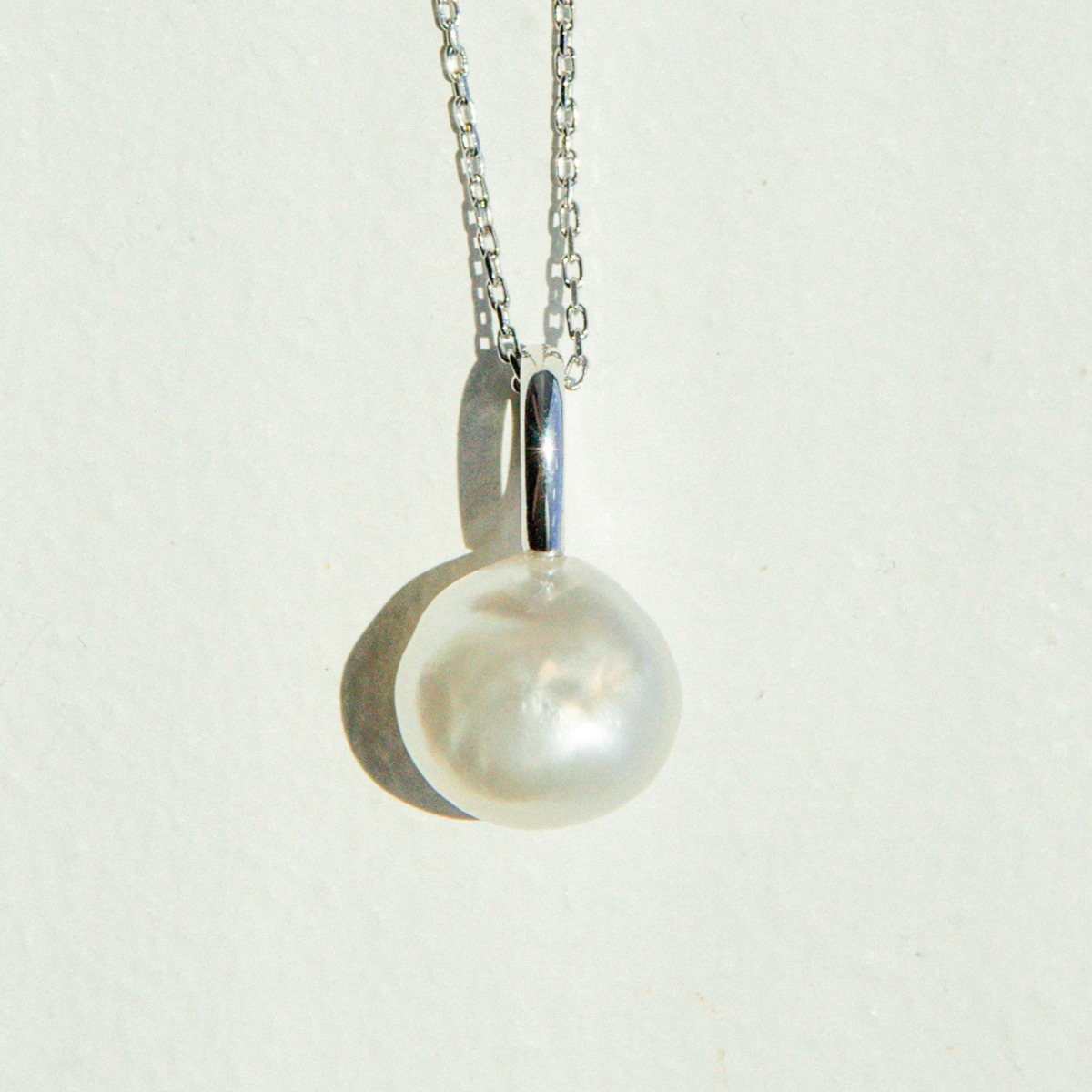 Pearl necklace with a silver chain on a light gray background