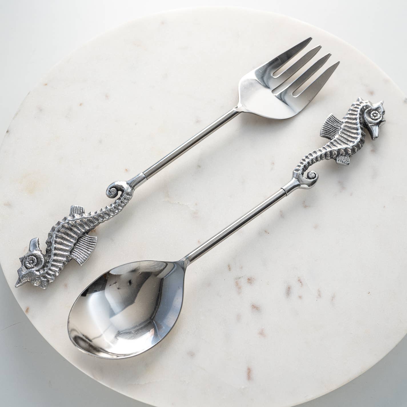 Serving spoon and fork with seahorse handles on a marble surface