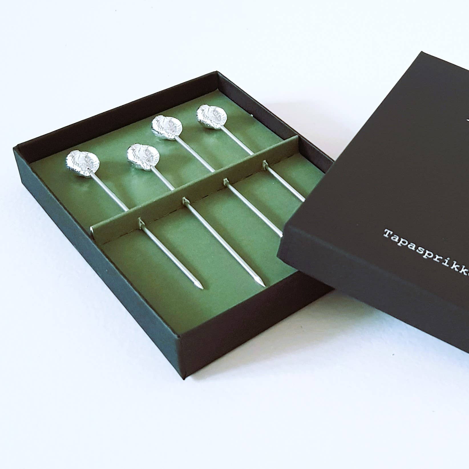 These tapas sticks are perfect for enjoying small snacks and easily extracting shellfish from their shells. Crafted from pure tin and handcrafted in the Netherlands, they come in packs of four and are elegantly presented in a luxurious black box with a sophisticated green sleeve.