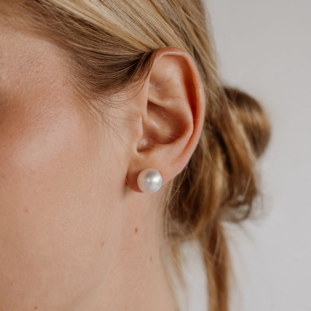 A woman wears her beautiful round Australian South Sea pearl studs set in solid gold.