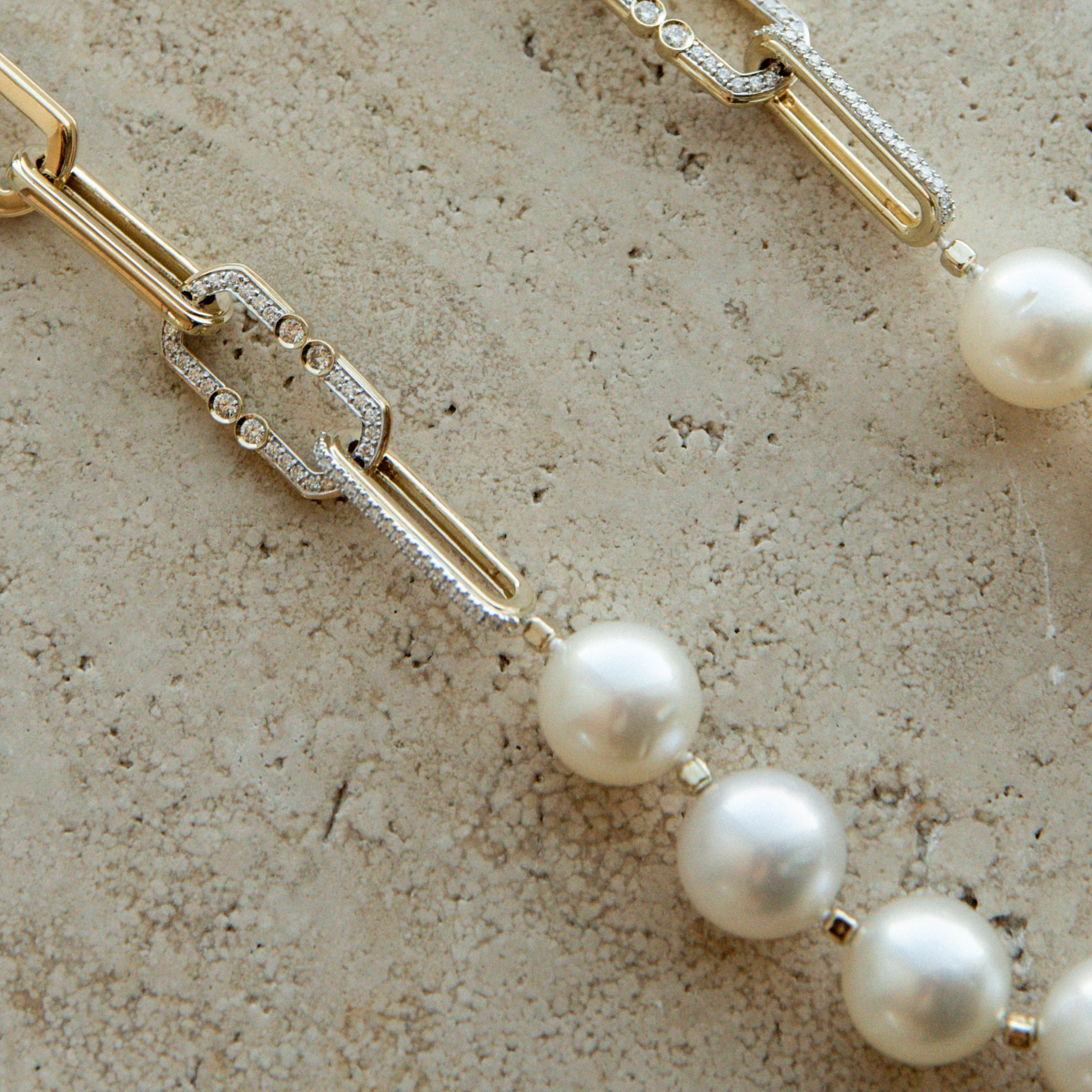 Australian South Sea Pearl necklace with gold paperclip chain and diamond accents on a beige stone surface