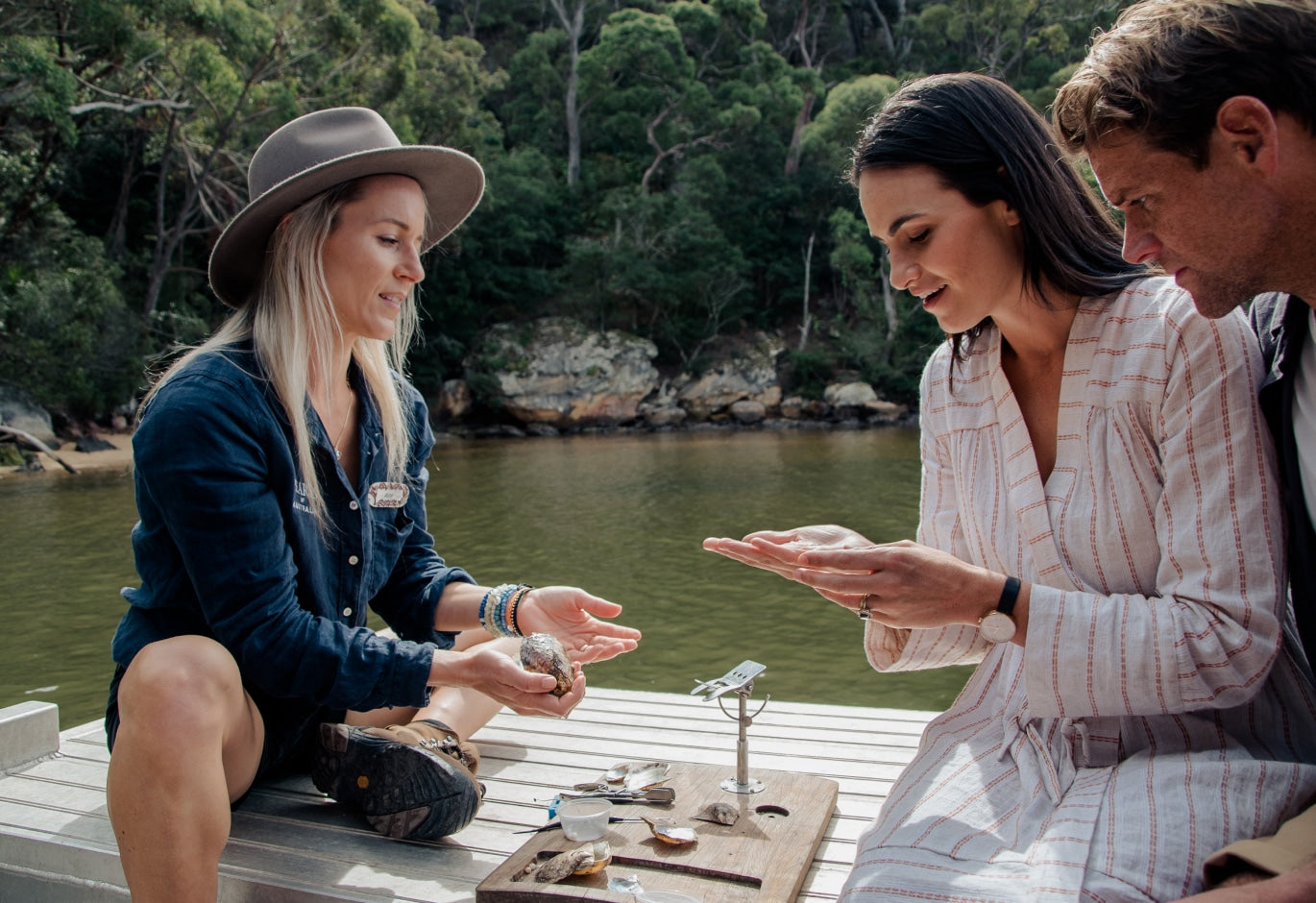 A tour guide sits on the side of a pearling vessel at our Broken Bay Pearl Farm with two guests showing them the process of harvesting the beautiful Akoya pearls from our Australian Akoya pearl oysters.