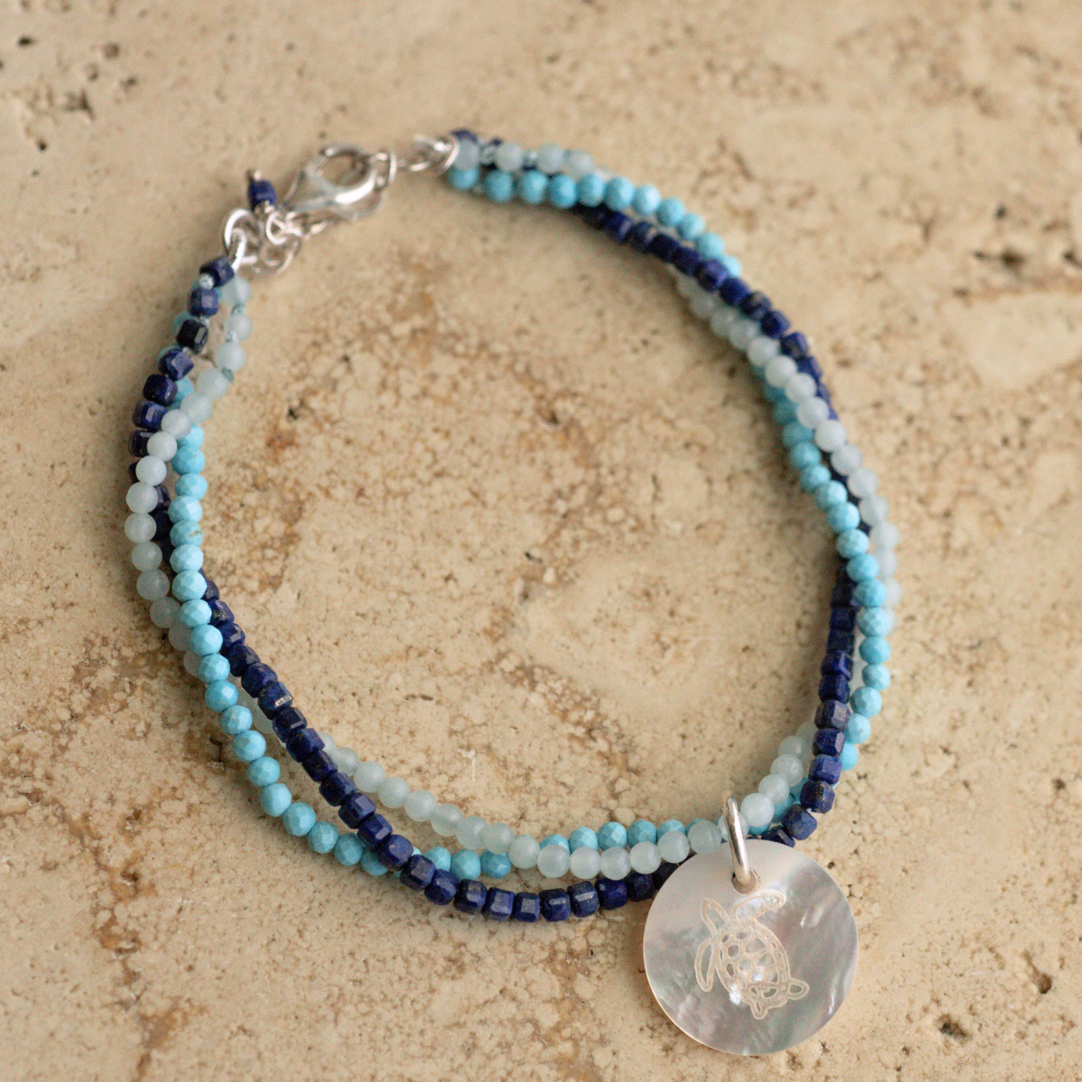 A unique Mother of Pearl charm bracelet featuring lapis lazuli, aquamarine, and turquoise gemstone beads, set in sterling silver.