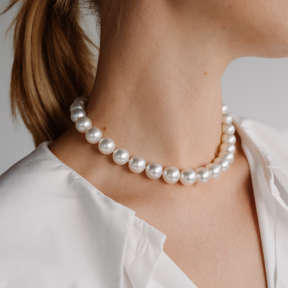 Pearl necklace worn by a person with a neutral background