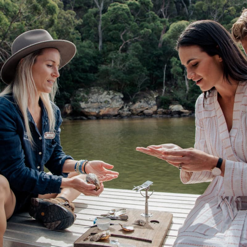 A tour guide sits on the side of a pearling vessel at our Broken Bay Pearl Farm with two guests showing them the process of harvesting the beautiful Akoya pearls from our Australian Akoya pearl oysters.