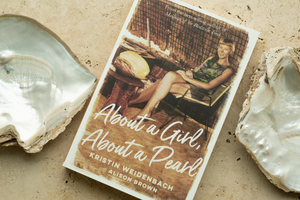 Photo of Alison Brown's memoir "About a Girl, About a Pearl" sitting alongside two Cygnet Bay grown Australian South Sea Mother of Pearl shells.