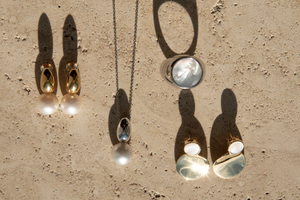 The Ebb collection sitting on a travertine surface, featuring Mother of Pearl, South Sea pearl pieces set in sterling silver and gold vermeil with high polish finishes.