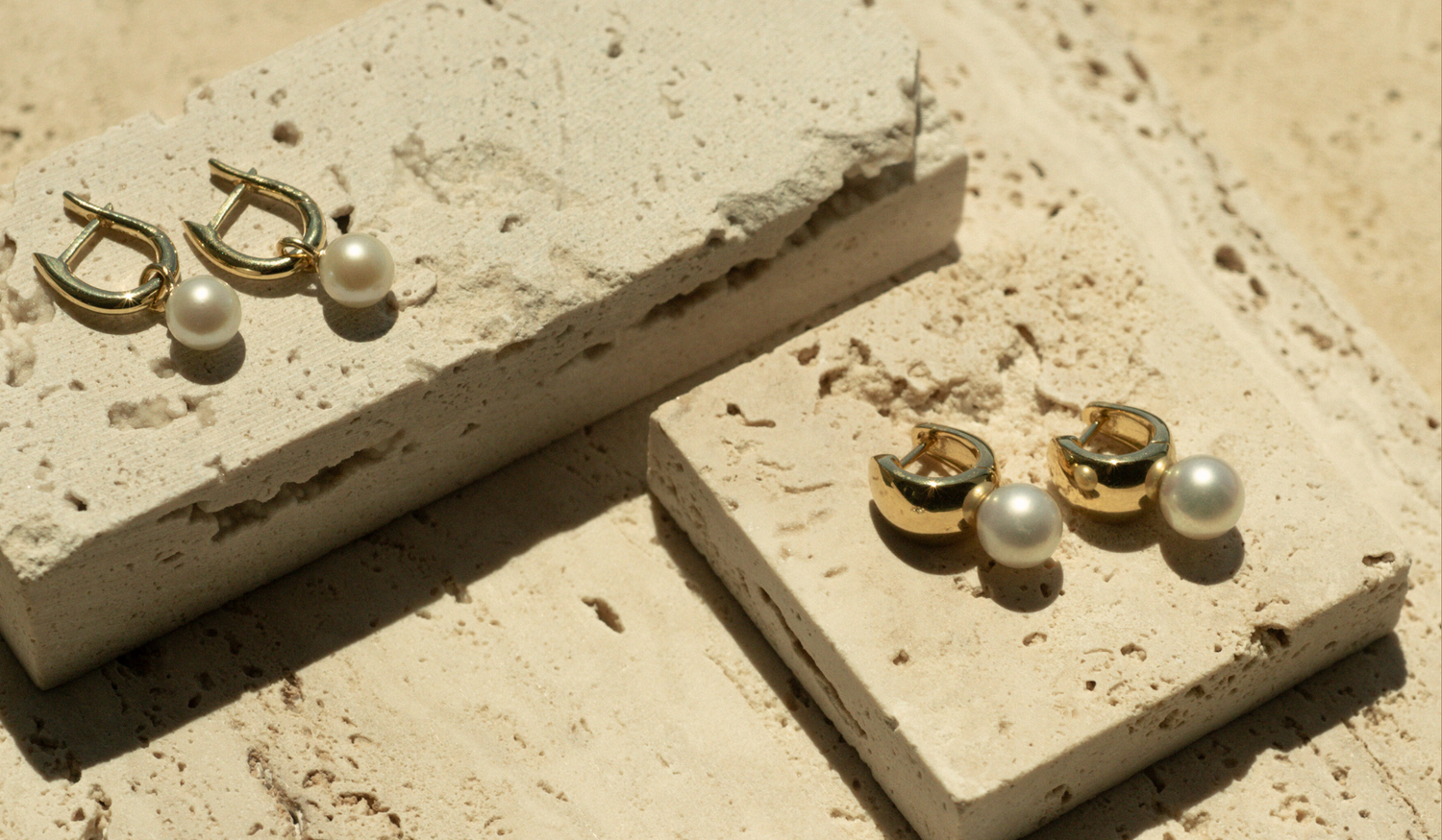 A pair of beautiful gold plated pearl huggies sit on a travertine tiles, each piece featuring lustrous pearls from our Broken Bay Pearl Farm shining in the natural light.