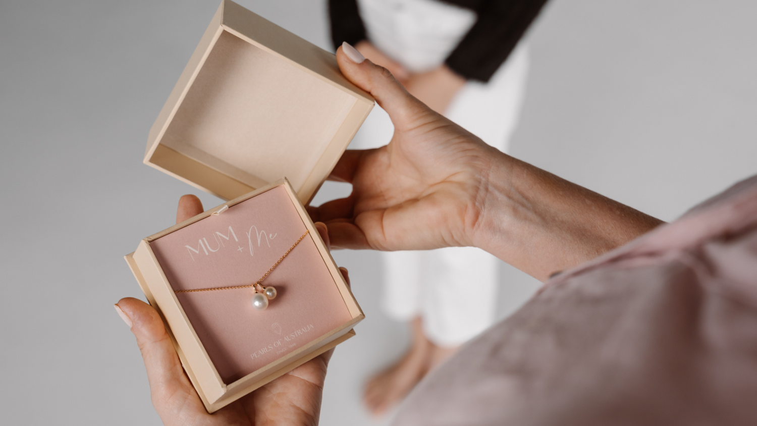 A woman holds her gift that features an Australian South Sea charm alongside an Australian Akoya charm hanging alongside.