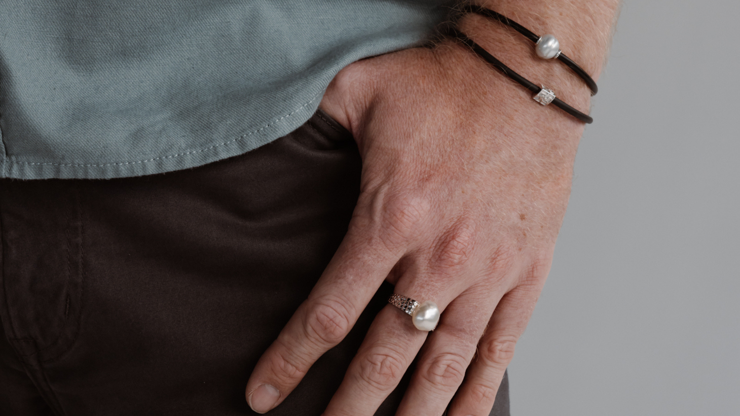 A man wears his Australian pearl jewellery gifts which include a Keshi pearl ring, and a stack of neoprene bracelets.