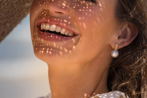 A woman smiles, wearing her stunning Impressions Studs that feature our Cygnet Bay grown Australian South Sea pearls.