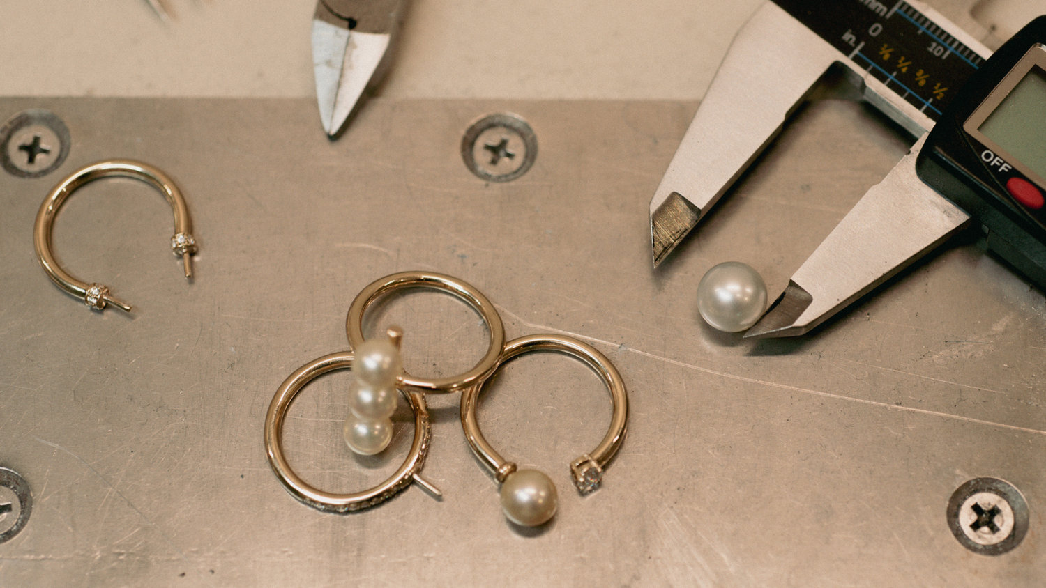 Several hand-crafted pearl rings sit on the jeweller's workshop table, ready to be crafted for a made to order piece.