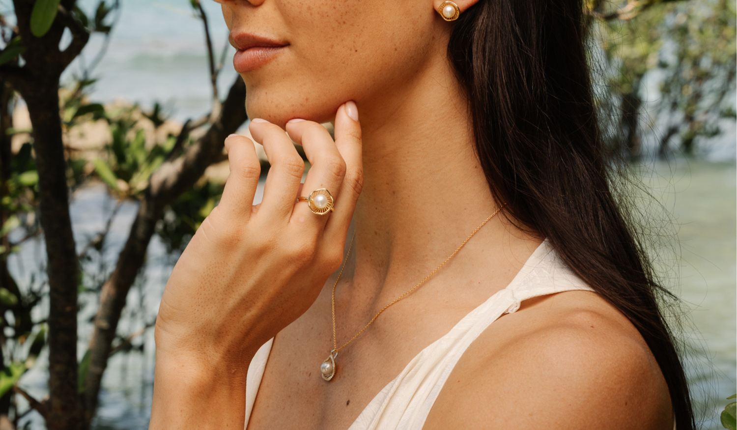 A model wears her stunning Mangrove Lily pearl jewellery set, featuring a pair of pearl studs and a pearl pendant designed in homage of the coastal marvel - the Mangrove Lily.