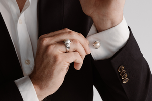 A man dresses in his suit before an event, putting on his Australian South Sea Mabe pearl ring and matching pearl cufflinks.