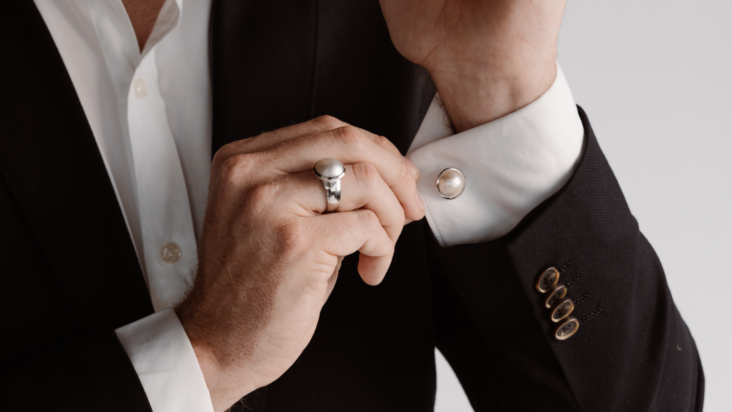 A man dresses in his suit before an event, putting on his Australian South Sea Mabe pearl ring and matching pearl cufflinks.