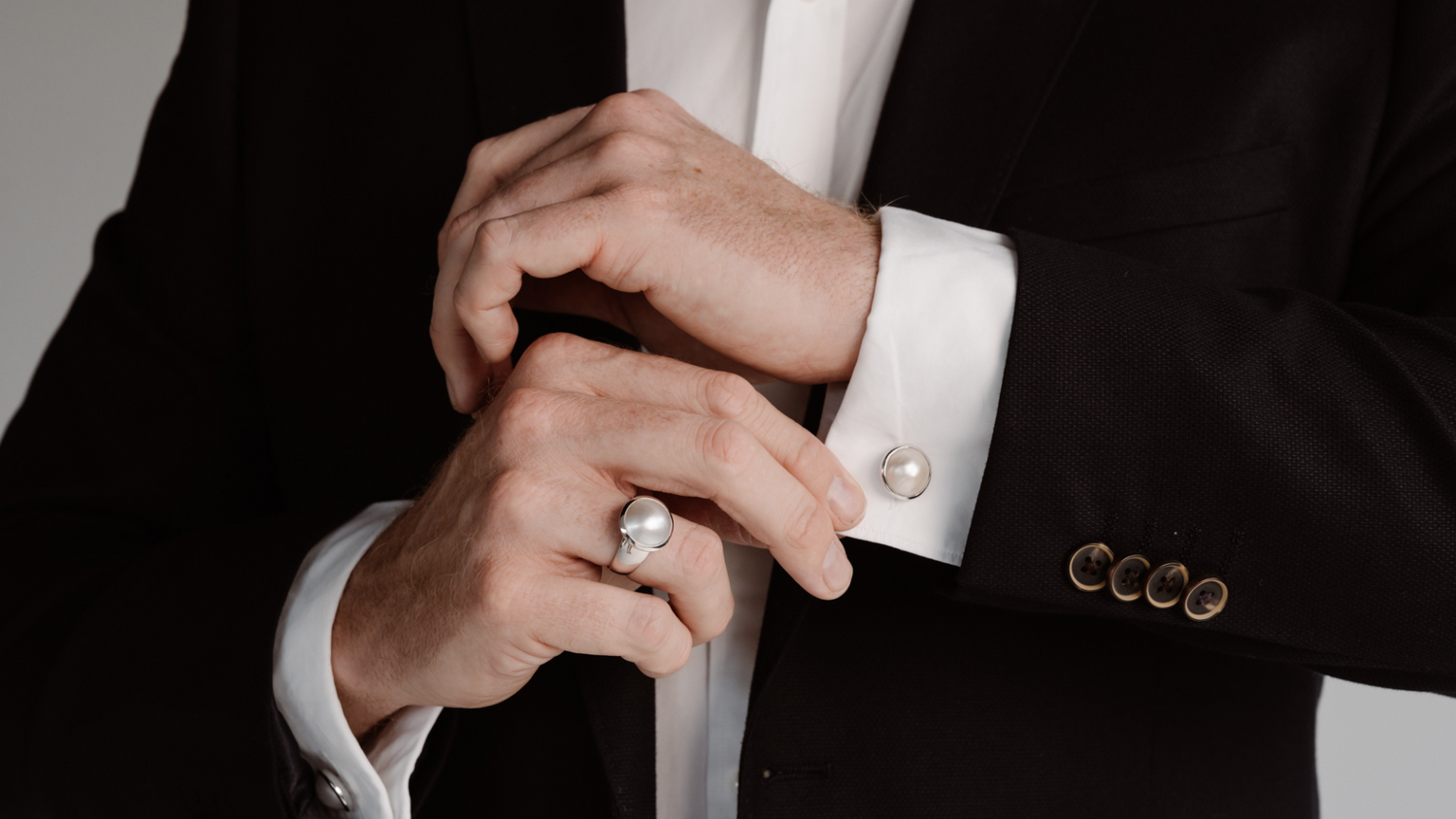 A man dresses in his suit before an event, putting on his Australian South Sea Mabe pearl ring and matching pearl cufflinks.