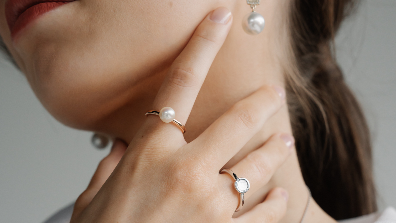 A woman wears her pearl jewellery, each featuring a different type of pearl. From her Mother of Pearl ring set in silver, alongside an Australian Akoya pearl ring set in gold and her Australian South Sea drop earrings set alongside diamonds.