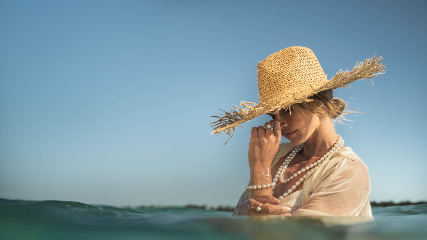 A woman stands in the turquoise waters of our Cygnet Bay Pearl Farm. She wears an array of Pearls of Australia jewellery pieces, including an exquisite pearl strand necklace with a matching pearl strand bracelet, as well as a pearl ring on each hand.